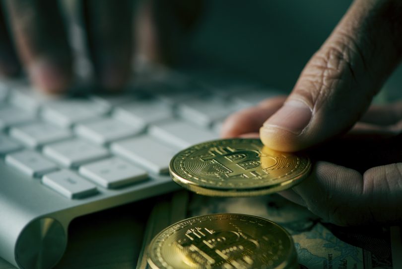 Tarragona, Spain - February 26, 2018: Closeup of a young man having a bitcoin from a pile of bitcoins while is using a computer