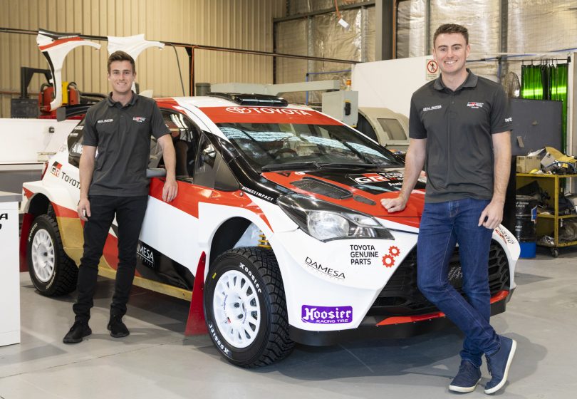 Lewis Bates and Harry Bates standing next to Toyota Yaris AP4 rally car in workshop.