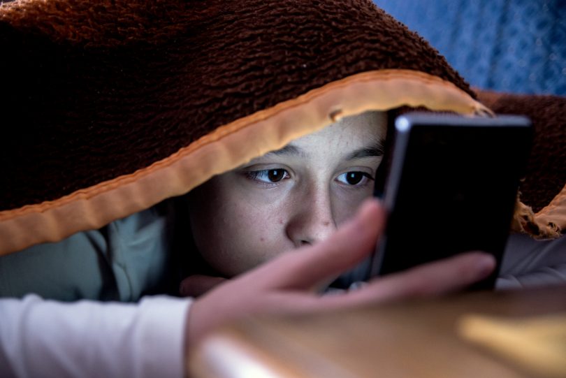 Girl under blanket on smartphone.