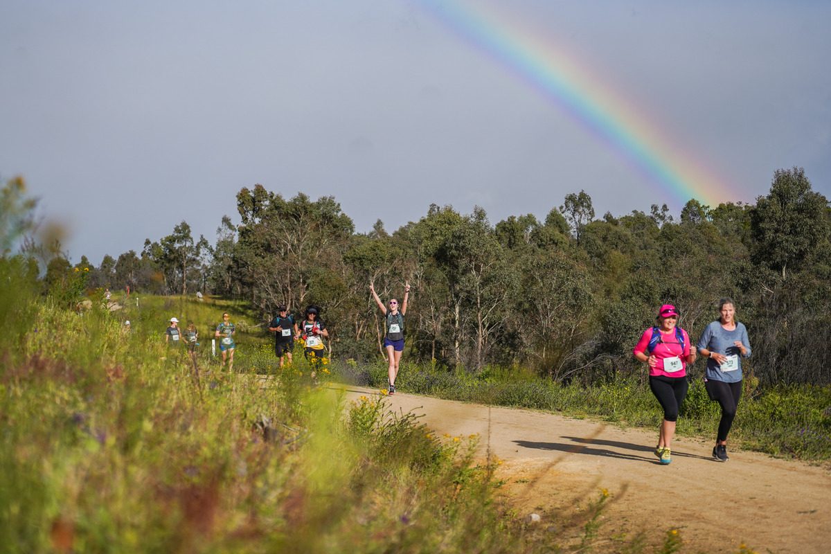 People at the Stromlo Running Festival jogging along a trail with a rainbow in the background.