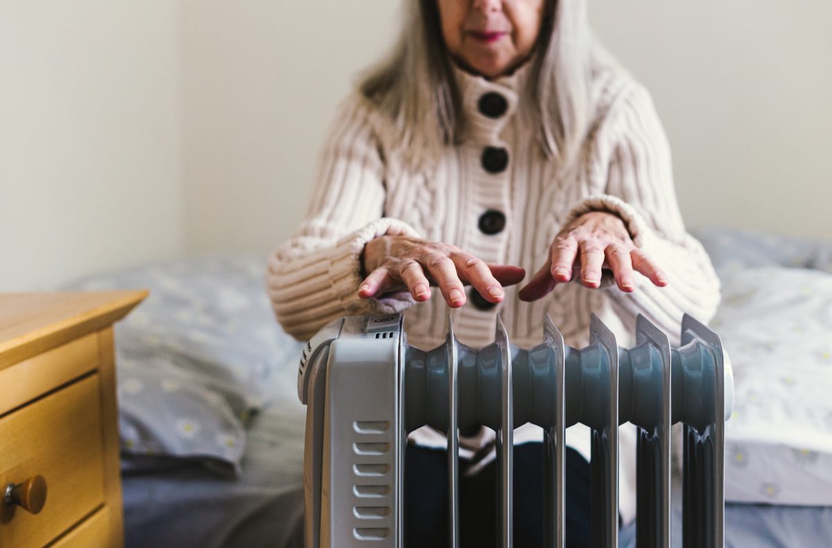 A senior warms her hands by a column heater