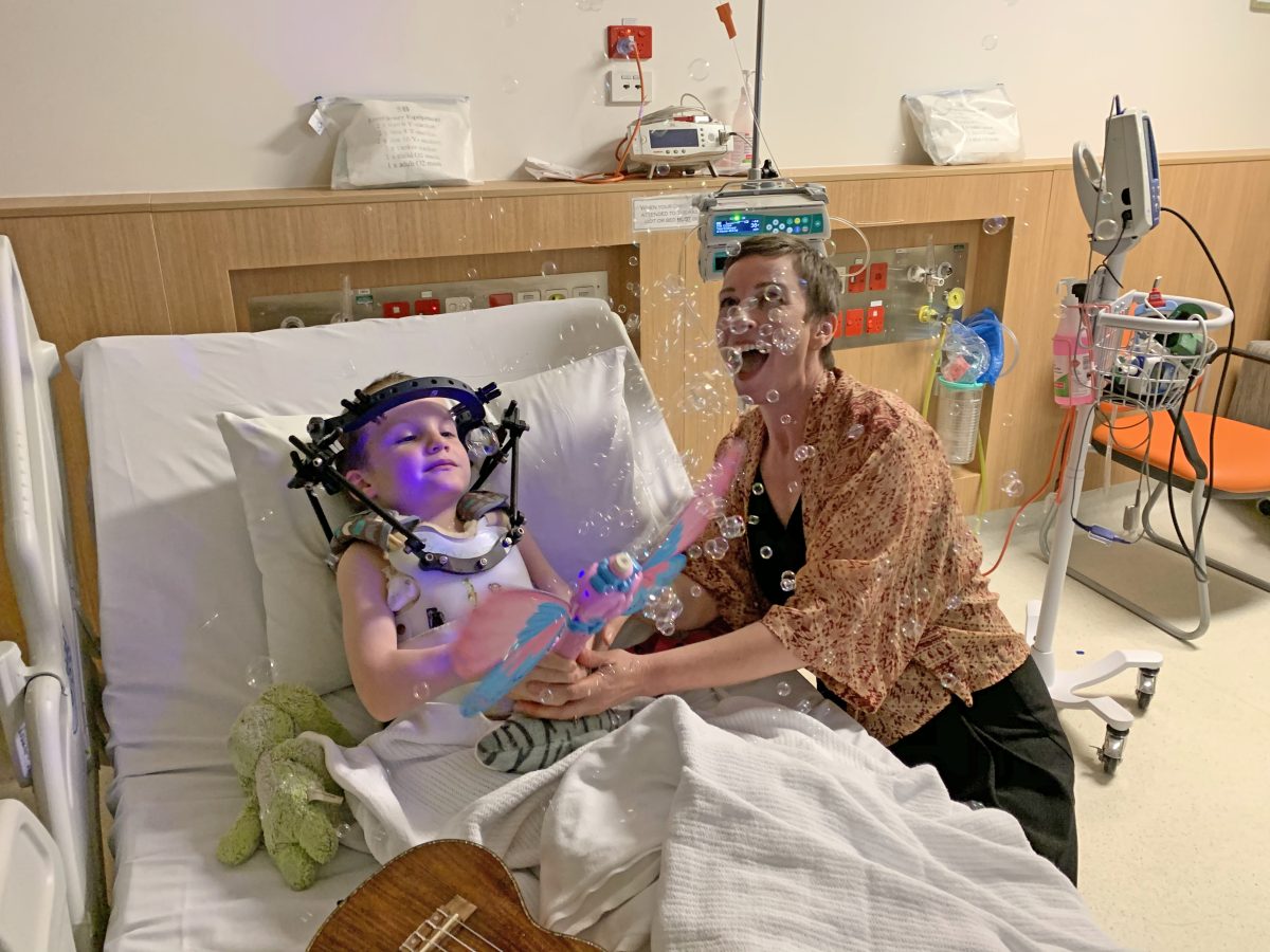 Lady playing with a bubble wand with a peadiatric patient in a hospital bed