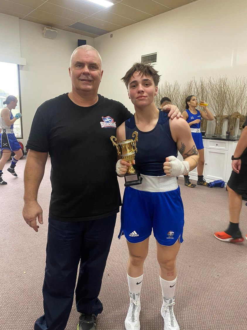 female boxer holding a trophy with her coach