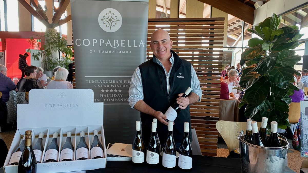 Man holds bottle of wine in front of Coppabella winery banner