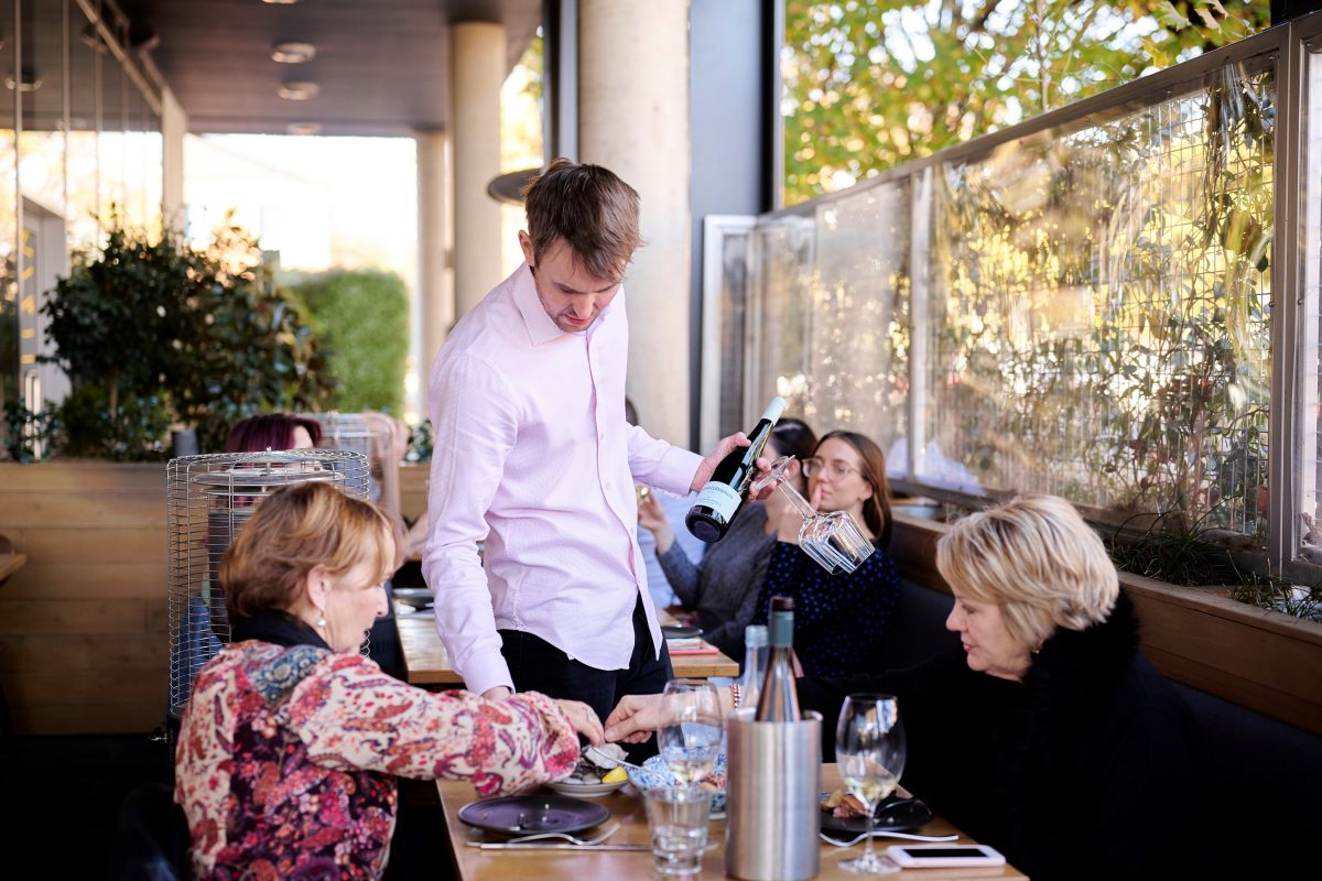 Man in white shirt offers wine to a table in restaurant.