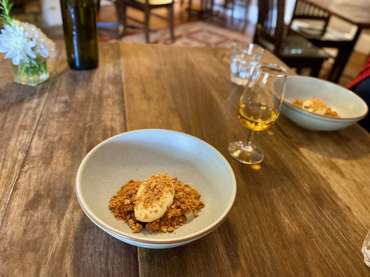 Bowl with toasted crumb and dollop of honey cream and a glass of a golden dessert wine on a wooden table