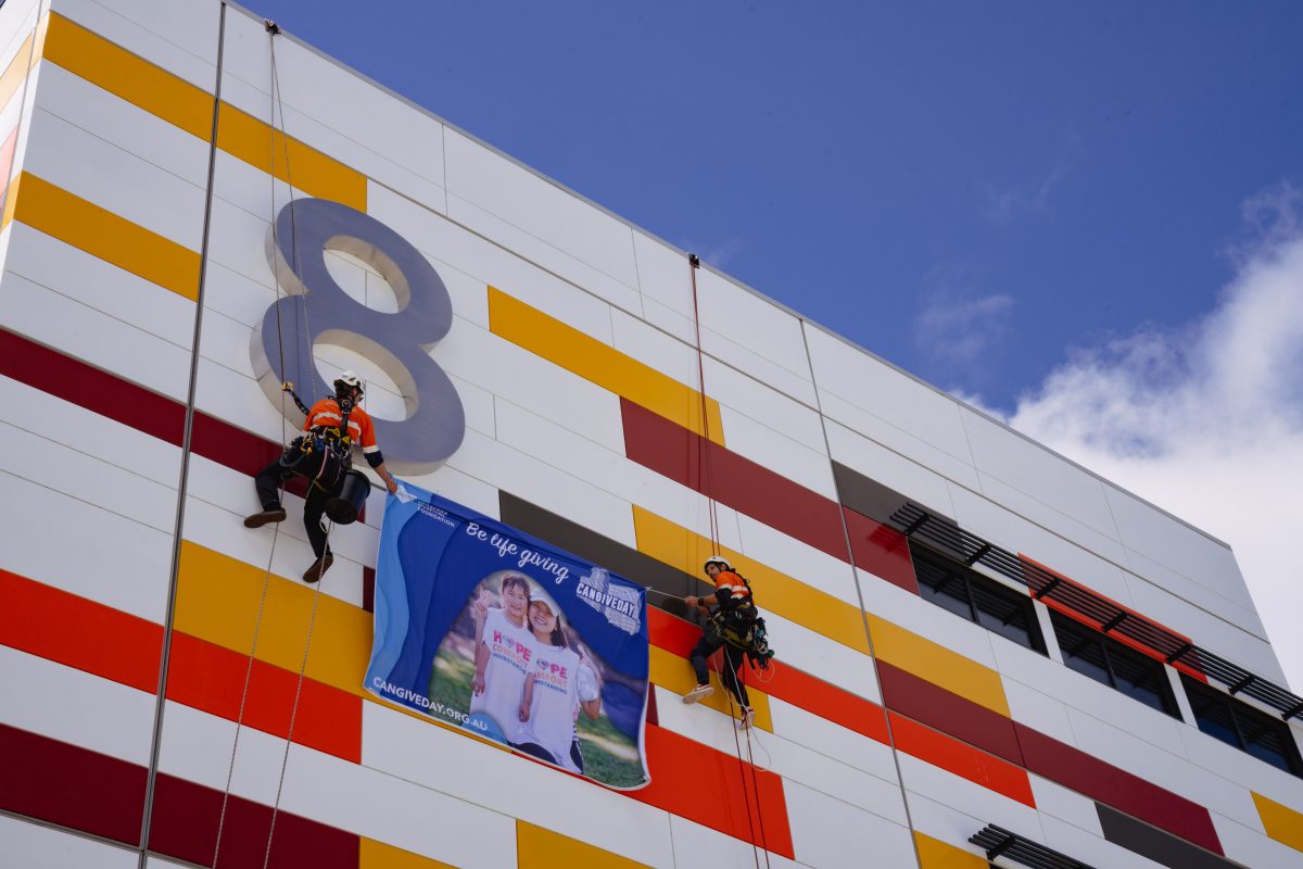 Two climbers rappel down a building to hang a giant Can Give Day sign.
