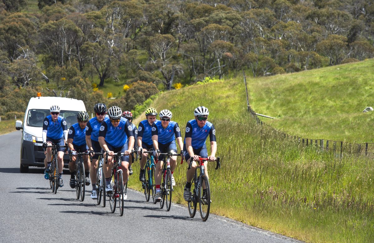 A group of cyclists riding up a hill with a van behind them during the day.