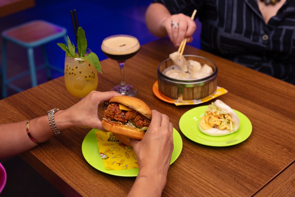 Hands holding burger in foreground and dumplings in background