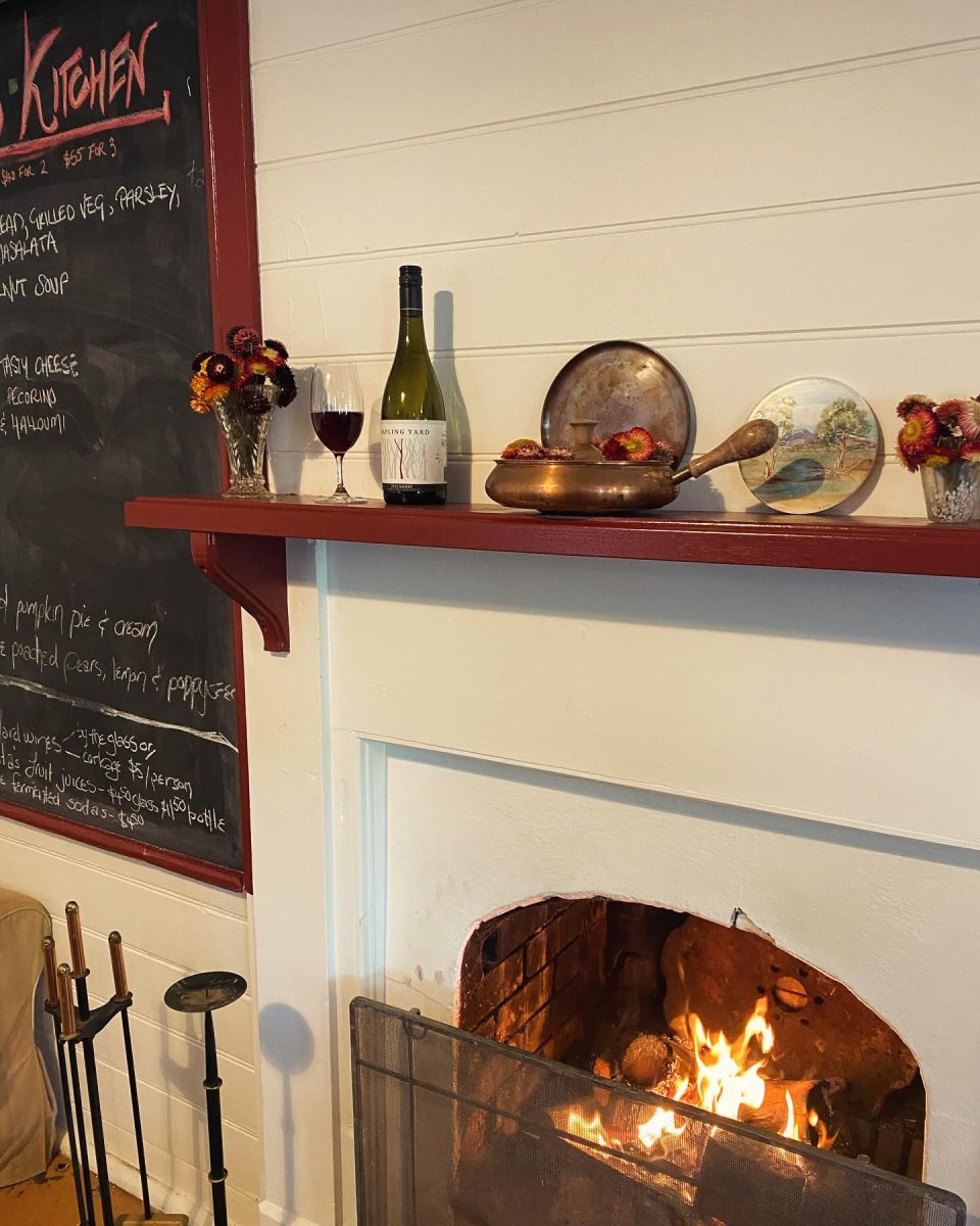 Bottle and glass of red wine on the mantlepiece of a roaring fire.