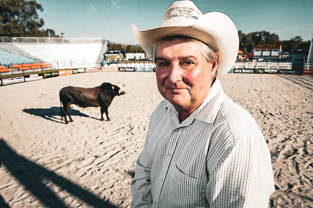 Man wearing cowboy hat with bull in background