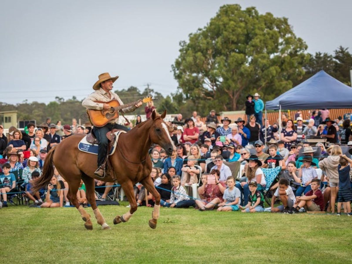 a man playing guitar whilst riding a horse in front of a crowd