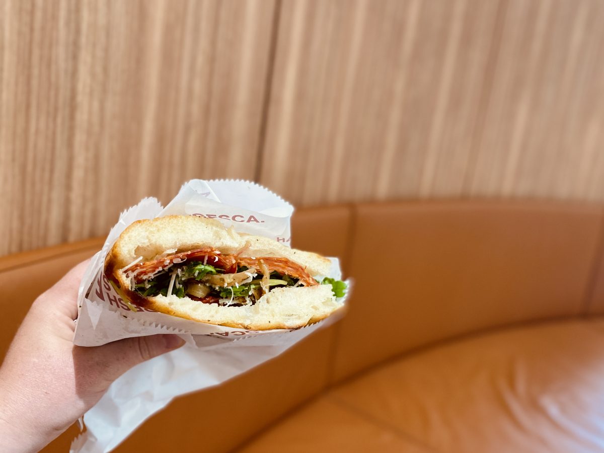 A hand holding a tasty looking sandwich with a reddish couch in the background. 