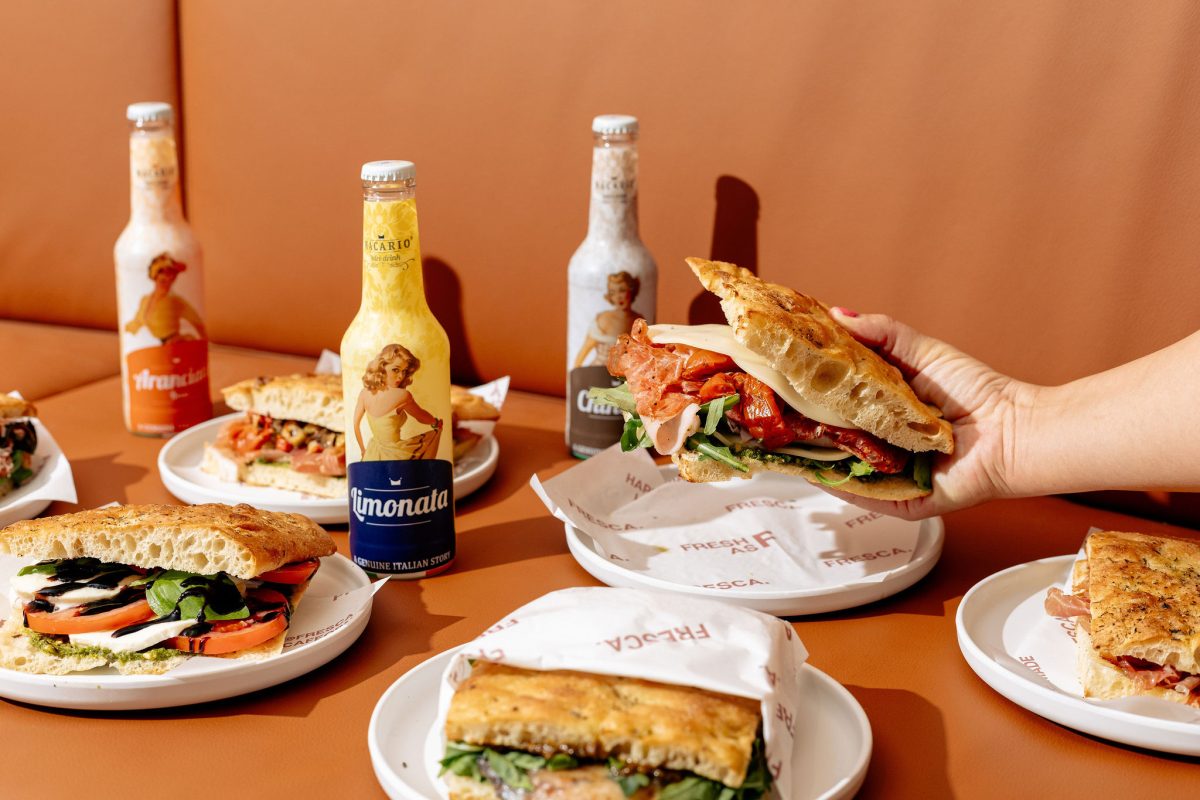 A group of sandwiches on a vibrant orange couch with several drinks. 