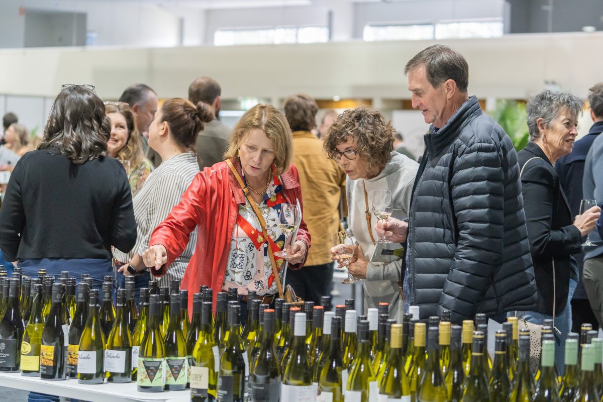 People at a wine tasting with dozens of bottles on the tables.