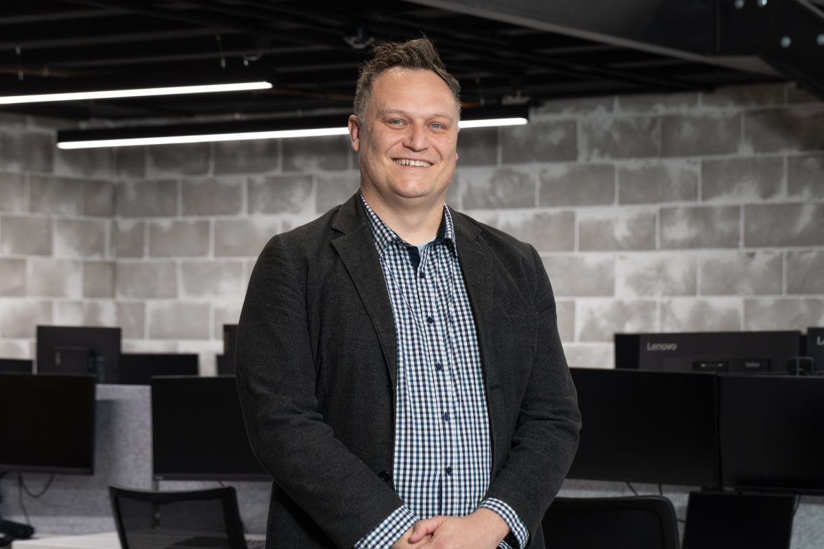 Man standing in front of computer desks and looking at the camera