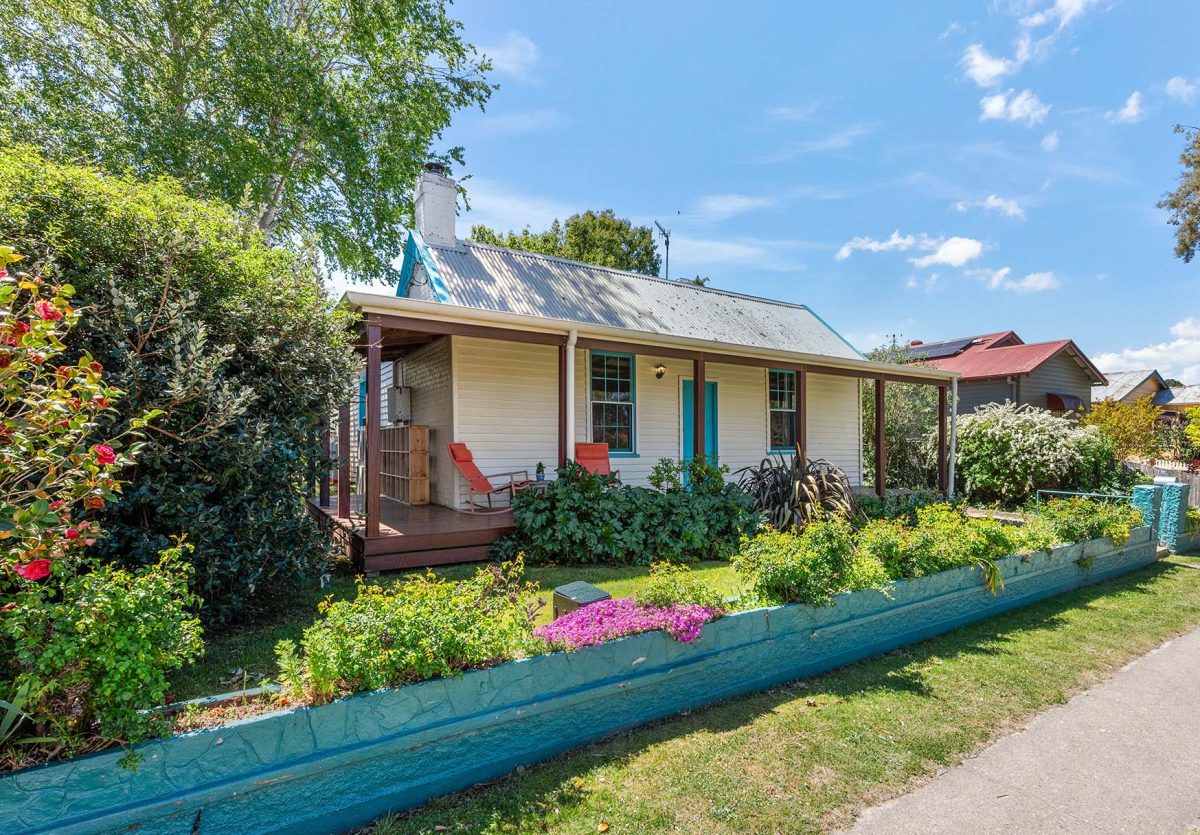 front facade of renovated cottage with lush gardens and blue highlights