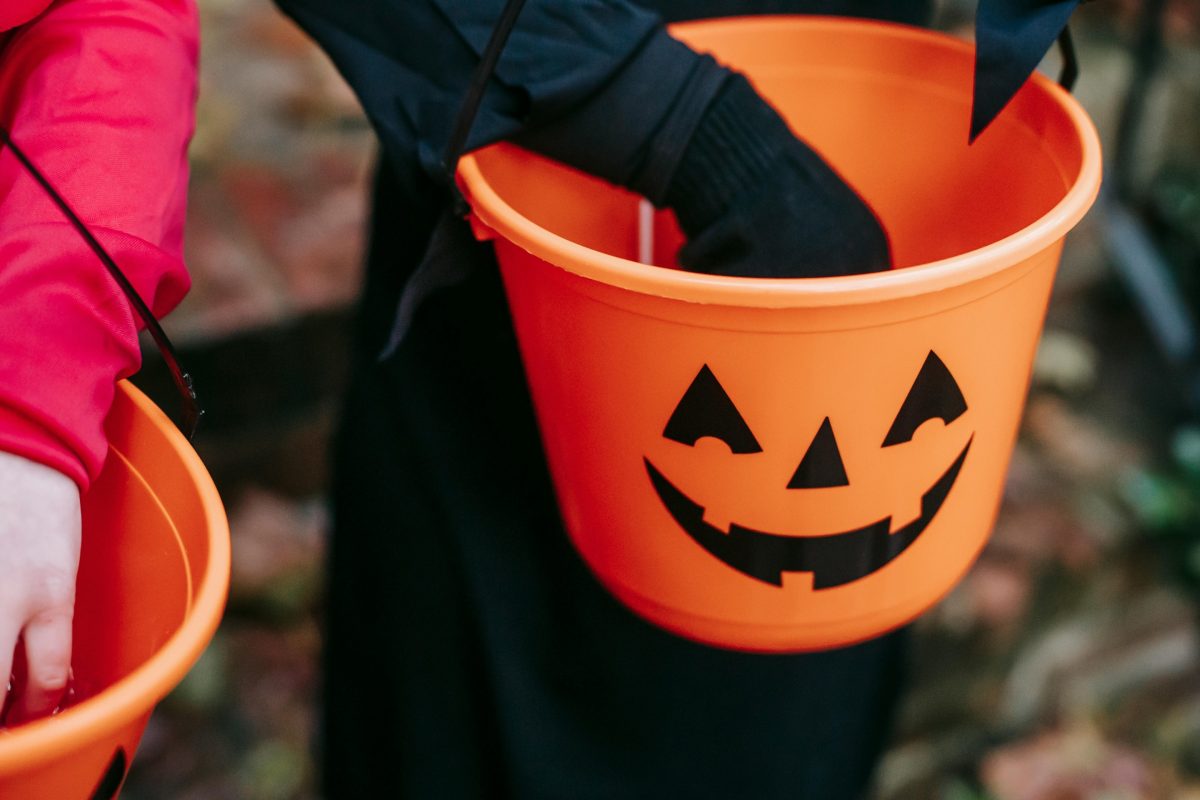 A close up of the hands of two children holding Halloween treat buckets.