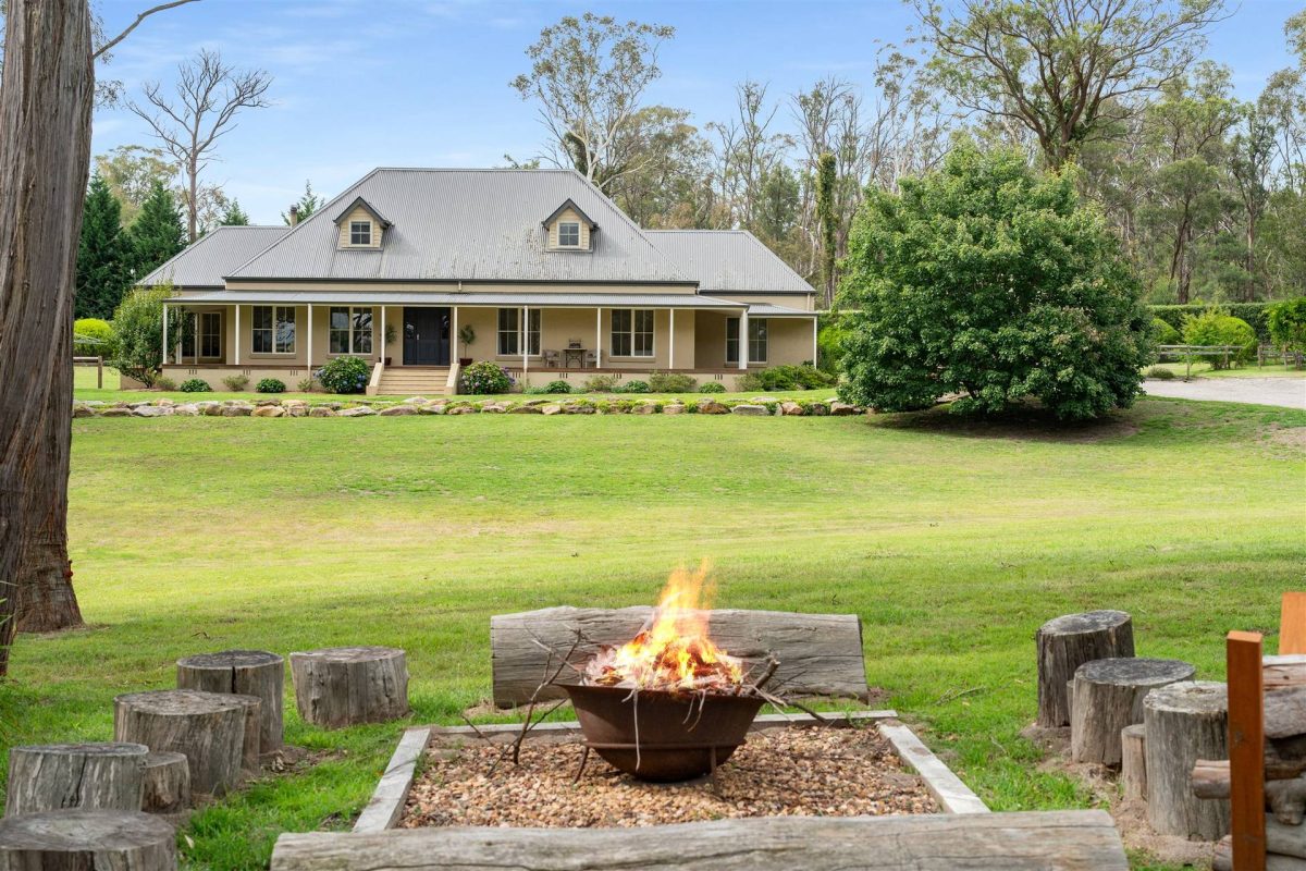 firepit area with log seats and colonial-style home in background