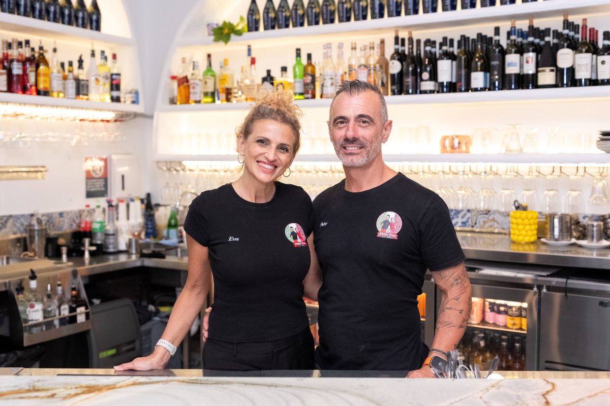 A smiling man and woman stand behind a bar together.