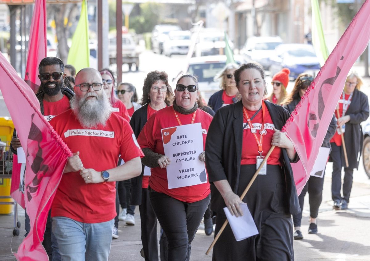 Union members walking the street in red shirts while holding flags.