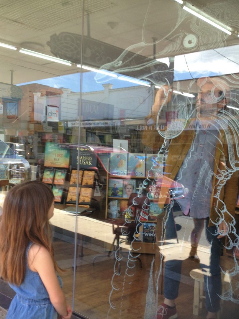 Bermagui-based artist Matt Chun is drawing an oversized cassowary made up of hundreds of tiny white lines and dots on the front window of Candelo Books in Bega. Photo: Elka Wood.