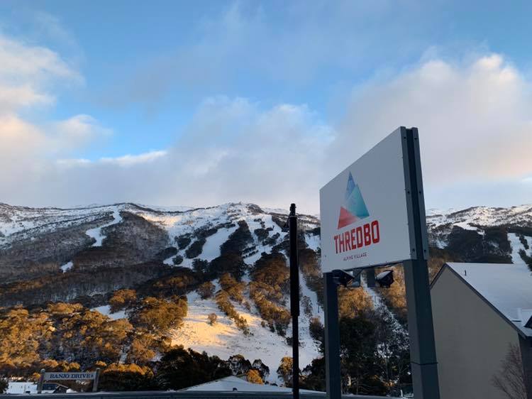 Thredbo sign in front of snow-covered mountains.