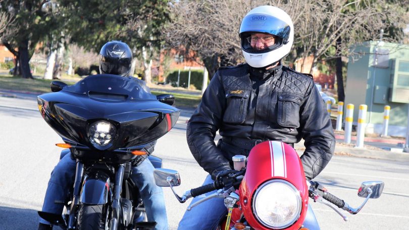 Two riders wearing helmets and motorcycle jackets, sitting on motorcycles.