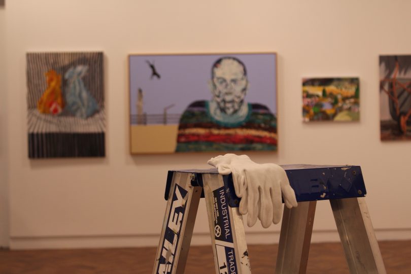 Ladder and gloves in foreground, hanging art in background at Goulburn Regional Art Gallery.