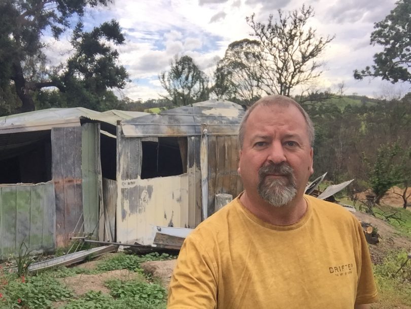 Andrew D'Arnay posing on rural property in front of fire-damaged shed.