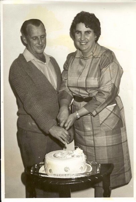 Tom and Pat Bourke, standing, cutting cake.