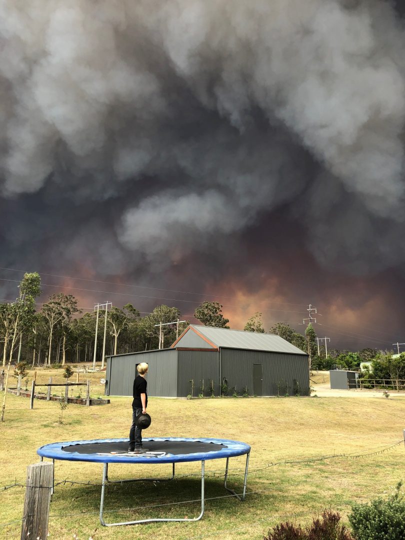 Boy on trampoline watching smoke from approaching bushfire.