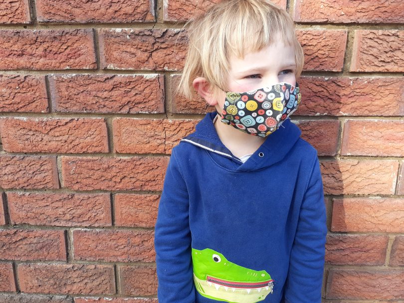 Child standing against wall wearing face mask.