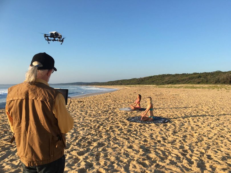 Man filming two models on beach by drone.
