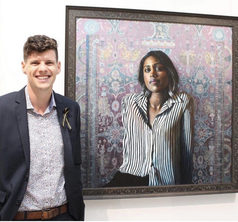 Cameron Richards standing next to his winning entry in the 2020 Shirley Hannan National Portrait Award.