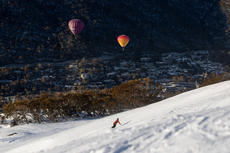 Two hot air balloons in air above ski field.
