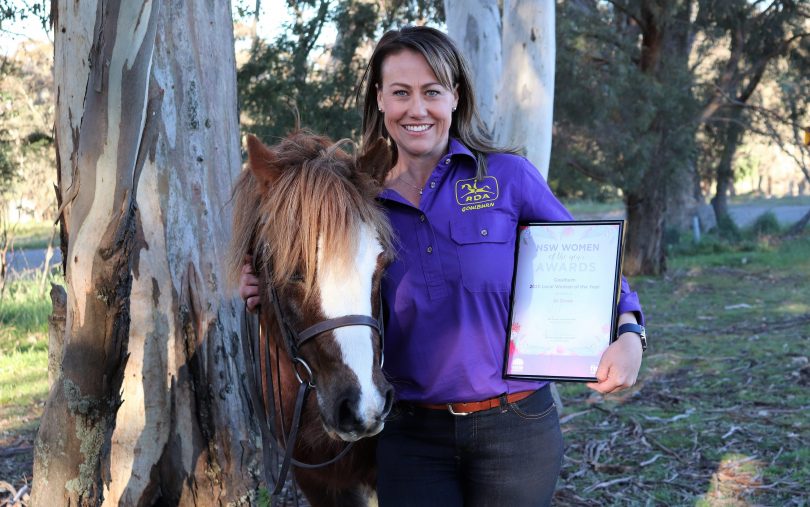 Jo Grove standing with pony showing off award certificate.