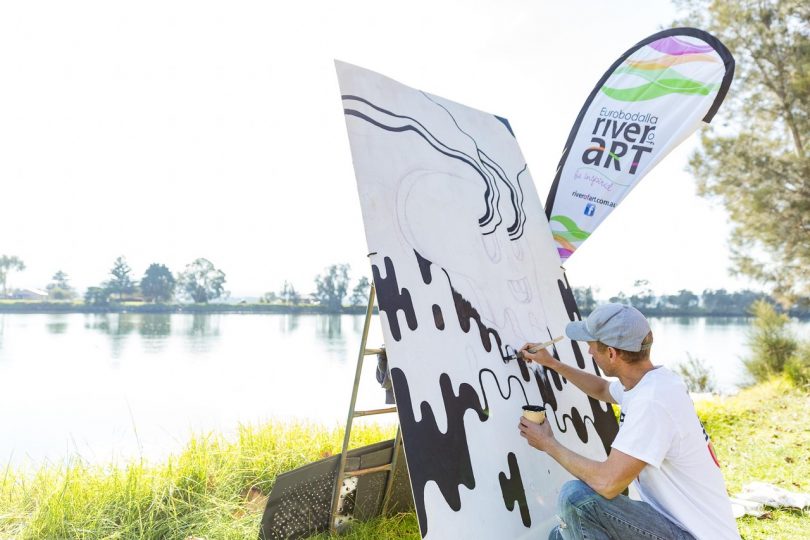 Artist painting by river as part of River of Art Festival.