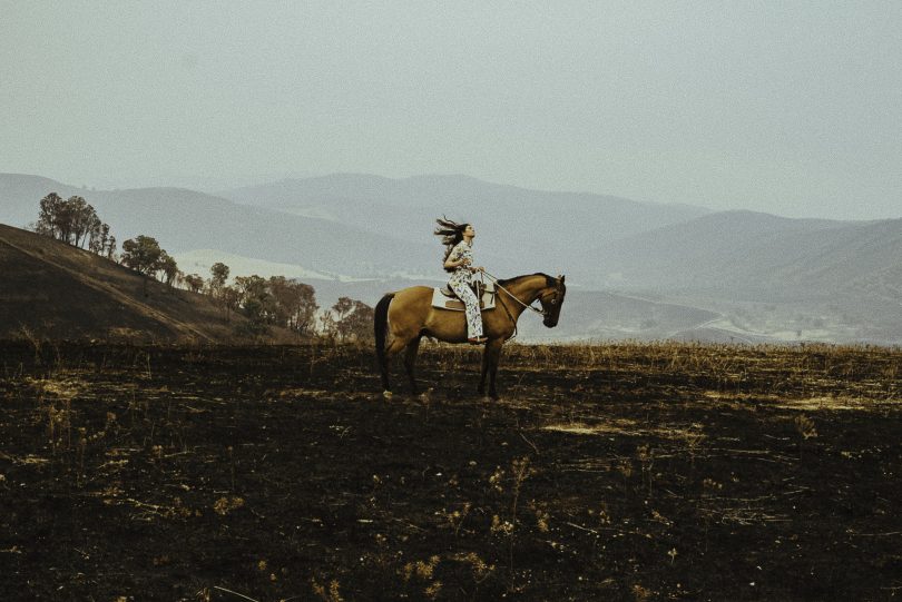 Fanny Lumsden on horseback on scorched rural land from bushfire.