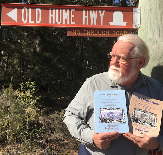 Stephen Gard standing beneath Old Hume Highway sign holding copies of book Once Upon a Hume.