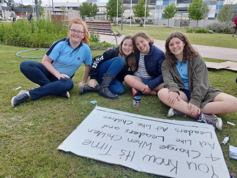 From left: Amalia-Grace Thompson, Jada Koek, Alina North-Andrew, Isha Constable, sitting on grass with climate-action sign.