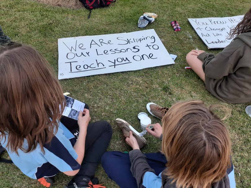 School students making climate-actions signs on grass.
