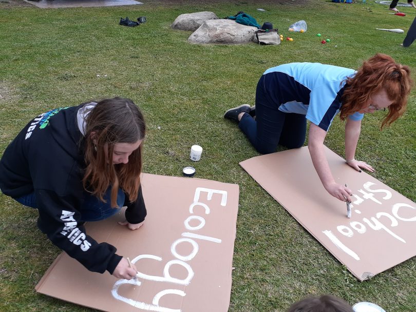 Jada Koek and Amalia-Grace Thompson making climate-action signs on grass.