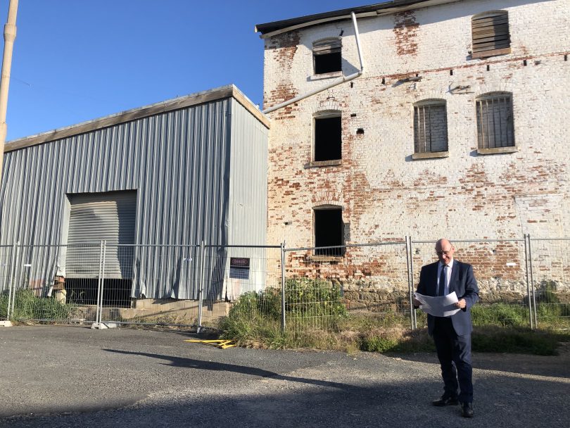 Michael McManus standing in front of Crago's Mill in Yass, reading plans.