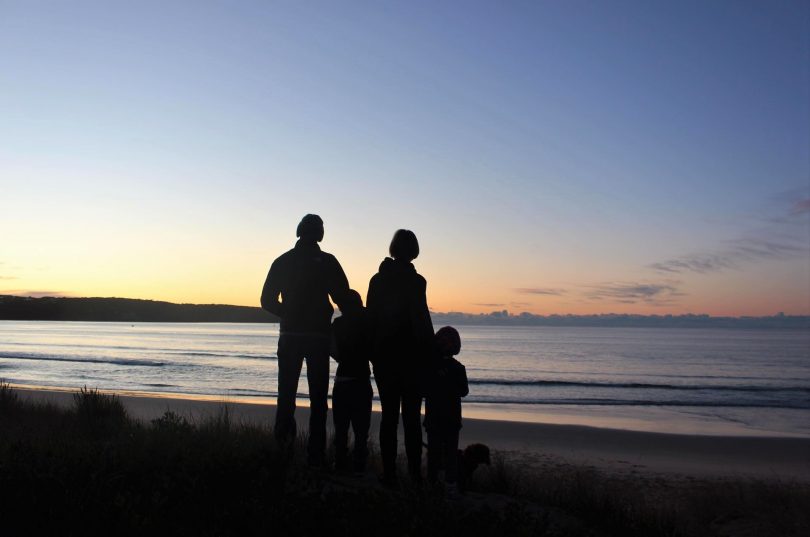Family standing on beach at dusk.