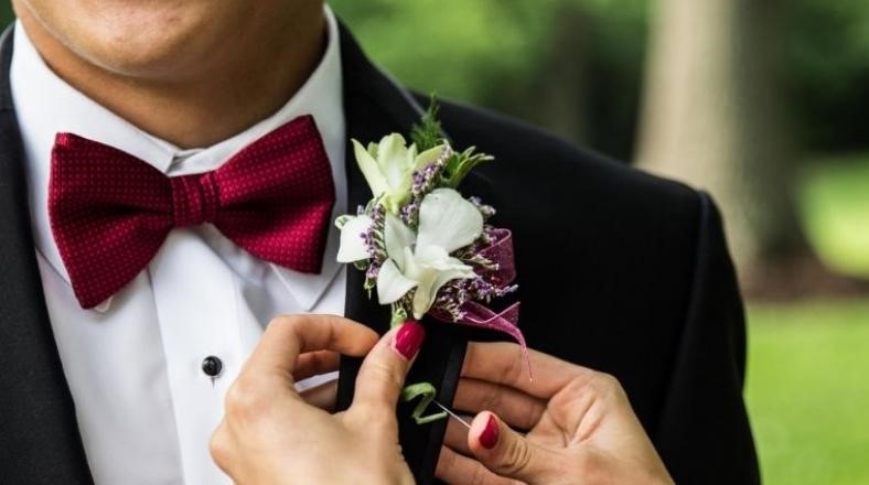 Woman's hands adjusting flower on suit being worn by man.
