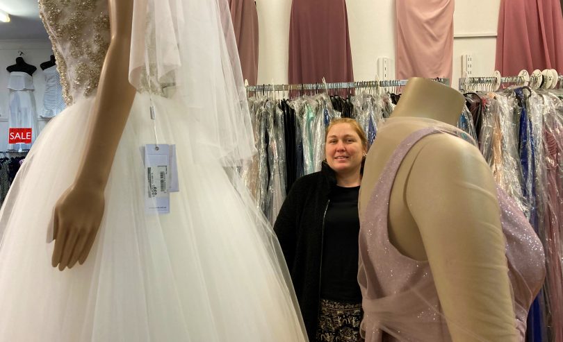 Tracey Chatto standing among formal dresses at Eve's Place Fashions in Moruya.