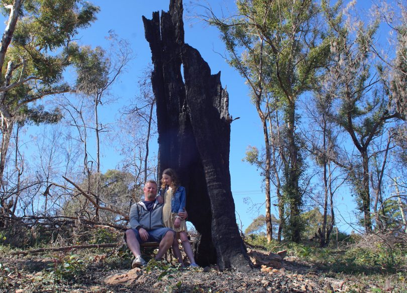 Jim Hughes and his daughter, Raeden, sitting next to burnt tree.