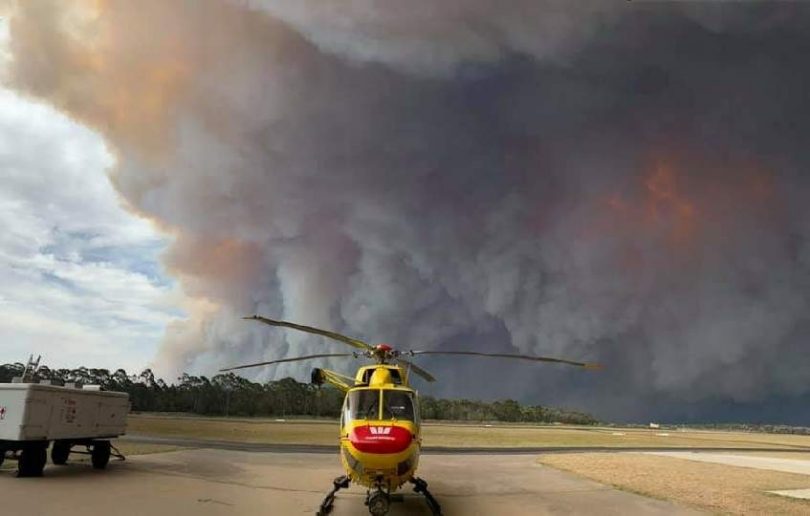 Rescue helicopter in foreground, bushfires in background near Broulee.