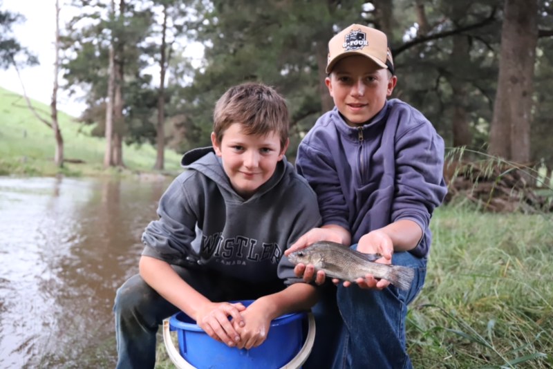 Bailey Piper and George Graham holding Macquarie perch fish beside river.